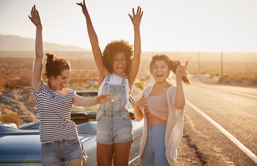 teenage girls cheering outside of car on road trip